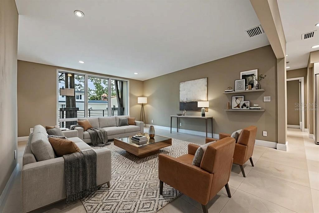A living room with light tile floors, neutral walls, a sofa, and two leather armchairs — 4909 W DRYAD STREET, TAMPA, FL