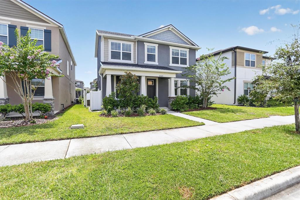 A two-story gray house with a covered front porch sits between two other suburban homes — 8565 LAMPPOST LANE, ORLANDO, FL