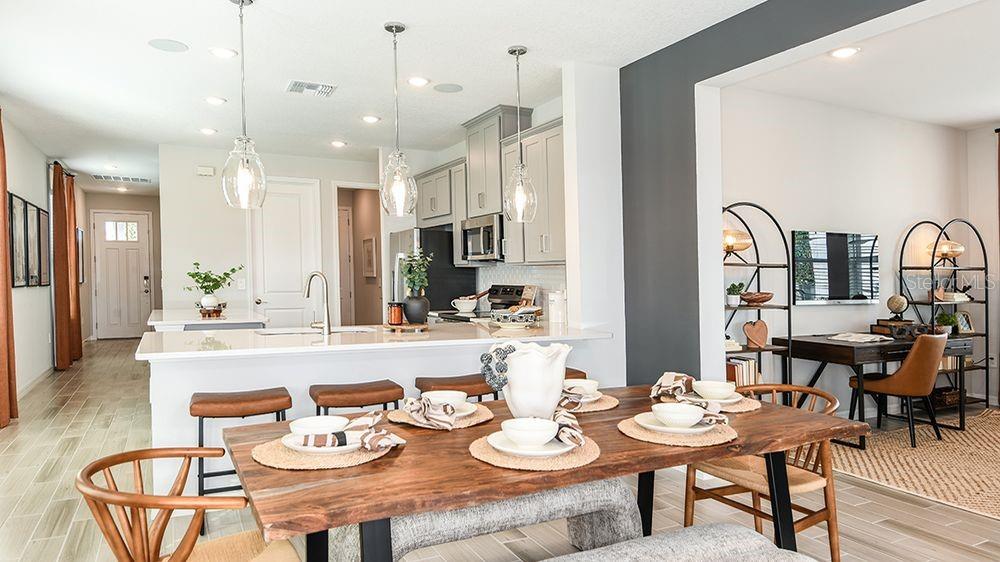 A dining area with a wooden table sits in front of an open-concept kitchen — 5795 PORTICO PLACE, KISSIMMEE, FL