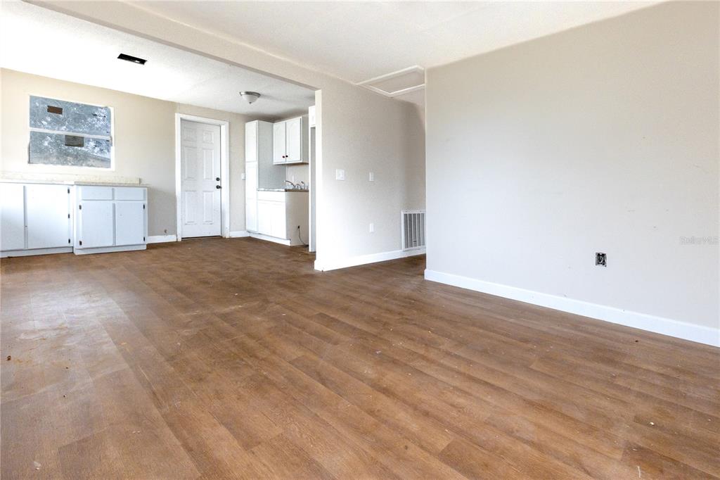 An interior view shows a living area with wood-look flooring leading to a kitchen — 642 PETERSON STREET, WAUCHULA, FL