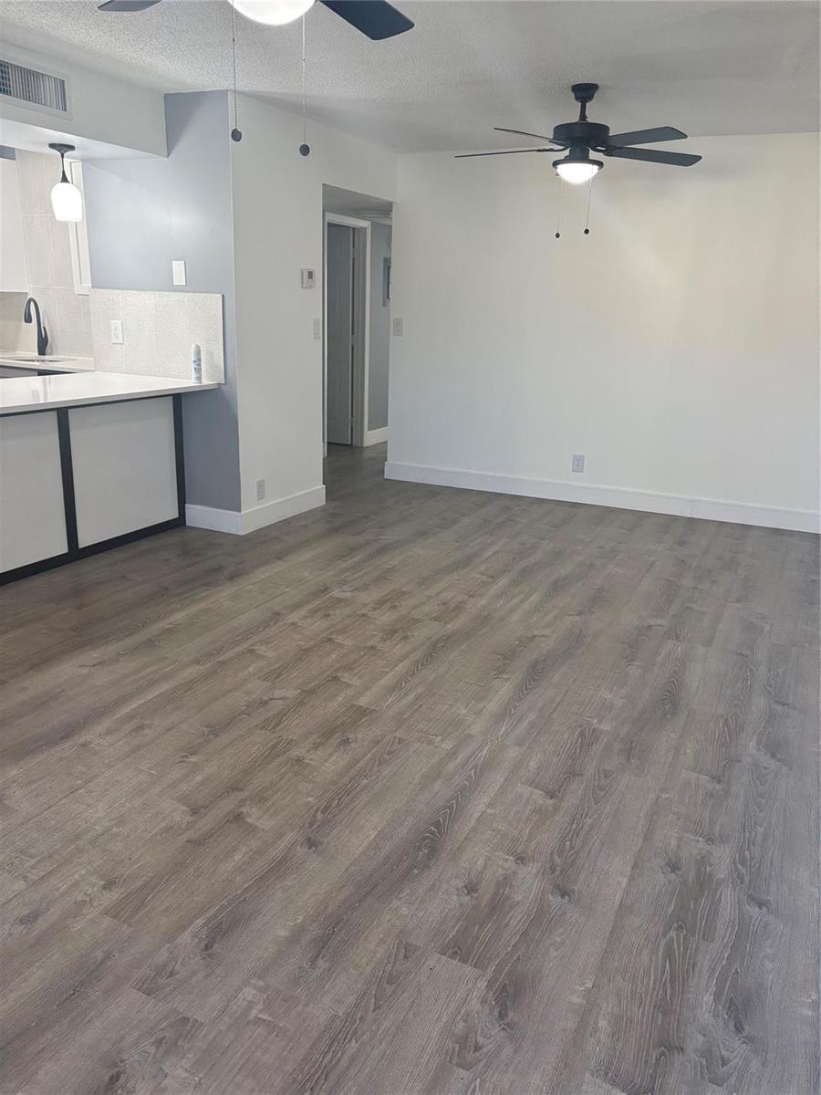 An open-concept living area features grey wood-look flooring, white walls, and a kitchen peninsula — 5492 Courtyard Drive # 5492, Margate FL 33063, MARGATE, FL