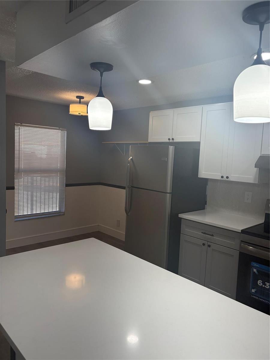 A kitchen features white upper cabinets, gray lower cabinets, stainless steel appliances, and pendant lighting — 5492 Courtyard Drive # 5492, Margate FL 33063, MARGATE, FL