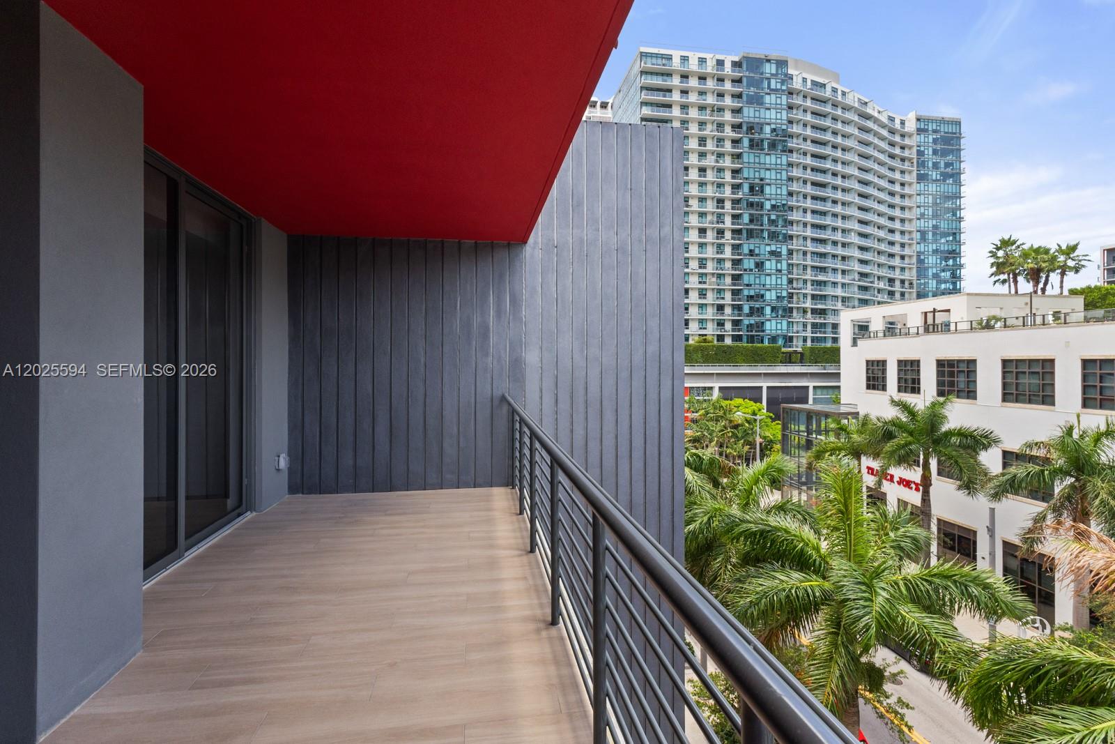 A modern balcony features wood-look tile flooring, a red ceiling, and a metal railing — 90 NE 32ND ST # 506, Miami FL 33137, MIAMI, FL