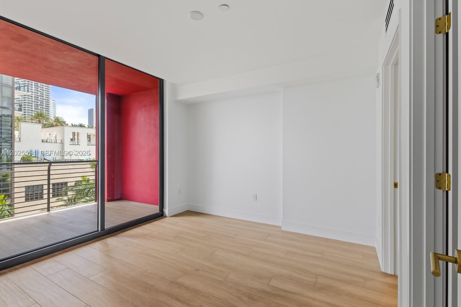 An empty room with light wood floors, white walls, and a balcony with red accents — 90 NE 32ND ST # 506, Miami FL 33137, MIAMI, FL