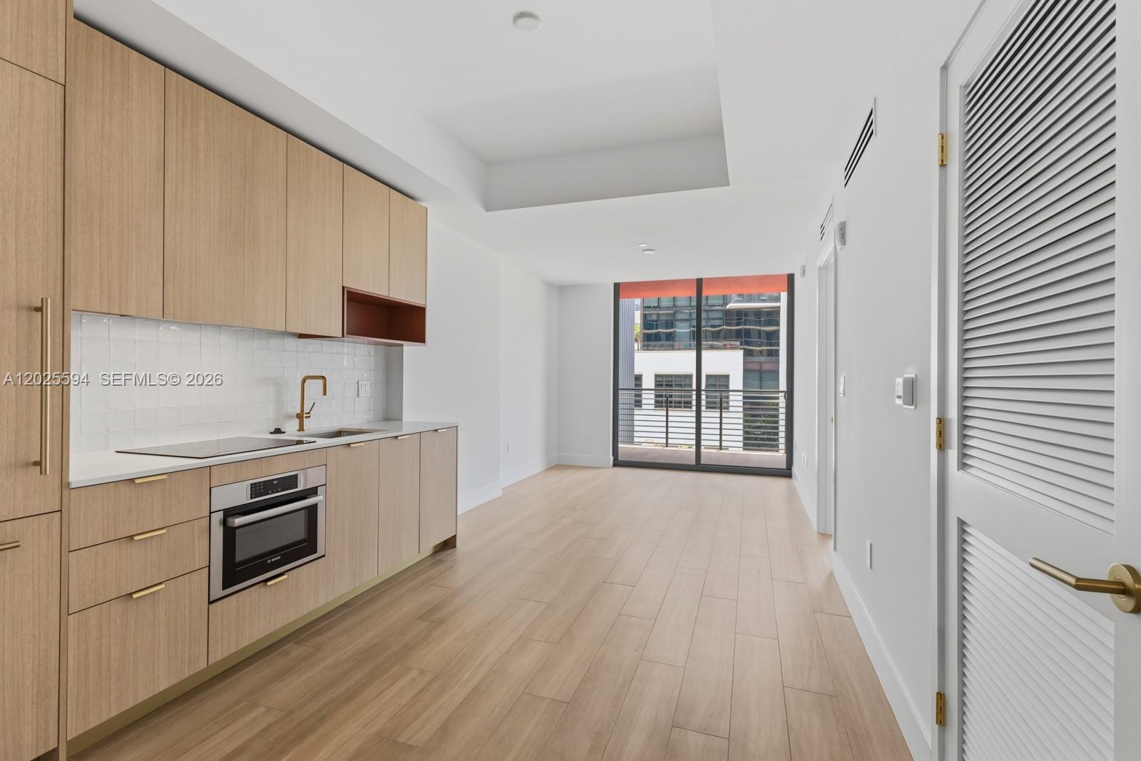 A modern kitchen with light wood cabinetry and white countertops opens to a balcony area — 90 NE 32ND ST # 506, Miami FL 33137, MIAMI, FL