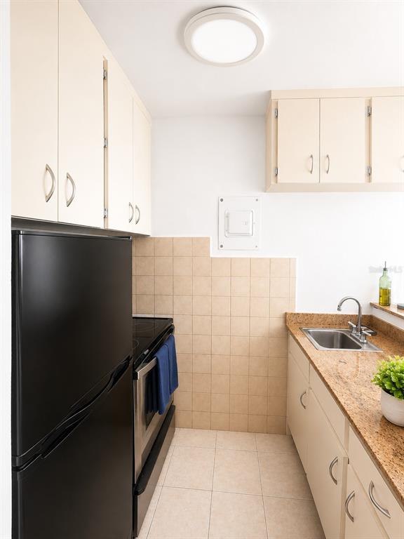 A galley kitchen features light-colored cabinets, granite countertops, a black refrigerator, and a stainless stove — 1452 MAGDALENA AVE UNIT 9C, SAN JUAN, PR