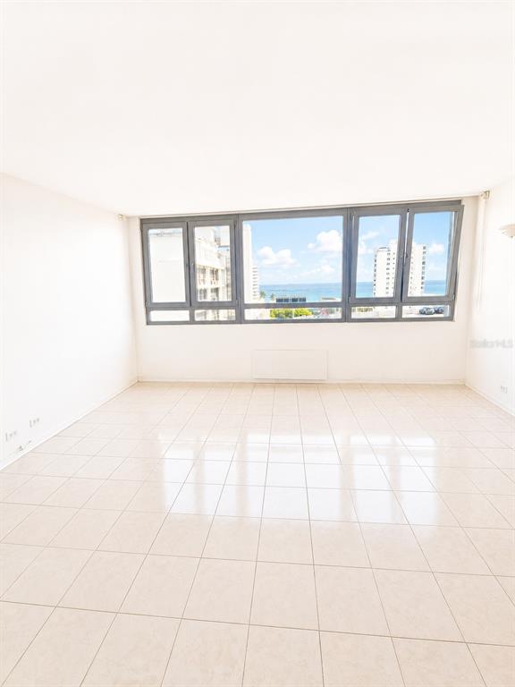 An empty room with light-colored tile flooring and a large window overlooking the ocean — 1452 MAGDALENA AVE UNIT 9C, SAN JUAN, PR