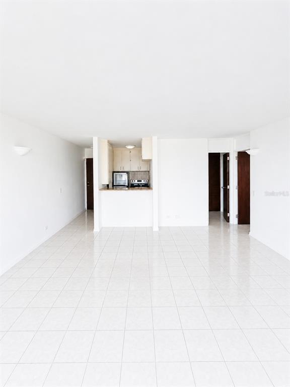 A bright, open-concept living area with white tile flooring leads to a small kitchen — 1452 MAGDALENA AVE UNIT 9C, SAN JUAN, PR