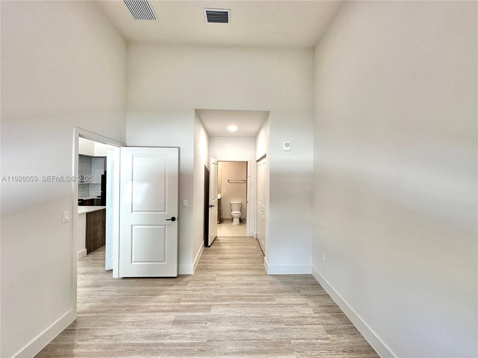 A bright room with light wood-look flooring leads to a hallway with a bathroom — 18412 Homestead Ave # 110, Miami FL 33157, MIAMI, FL