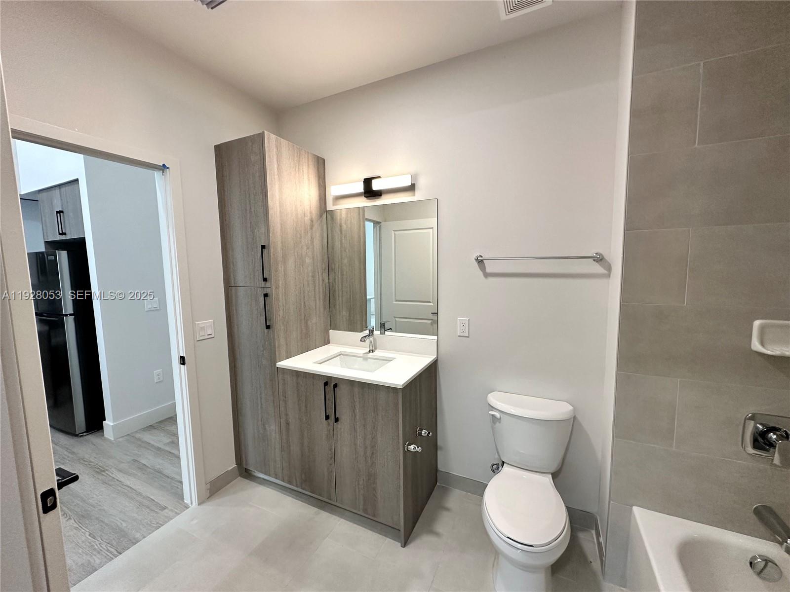 A bathroom features a wood-toned vanity, a toilet, and a tiled shower area — 18412 Homestead Ave # 110, Miami FL 33157, MIAMI, FL