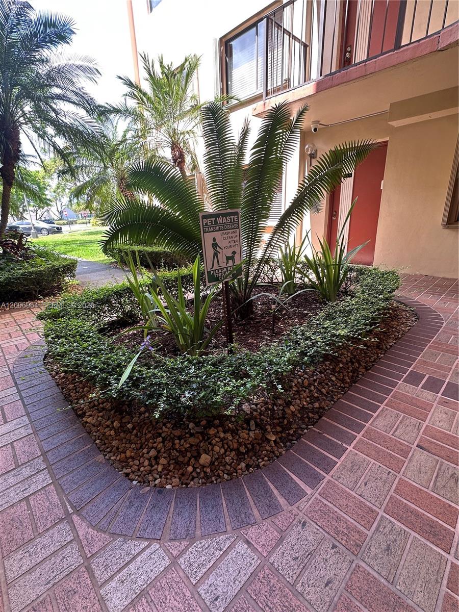 A small garden bed with a pet waste sign sits in front of a building entrance — 8700 SW 133rd Ave Rd # 109, Miami FL 33183, MIAMI, FL