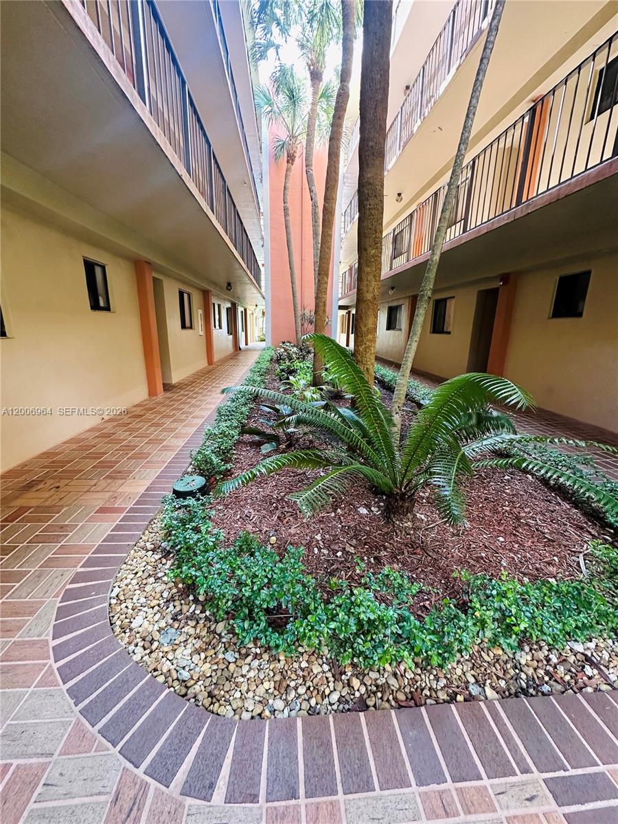 An outdoor courtyard features a central garden bed with palm trees and a tiled walkway — 8700 SW 133rd Ave Rd # 109, Miami FL 33183, MIAMI, FL
