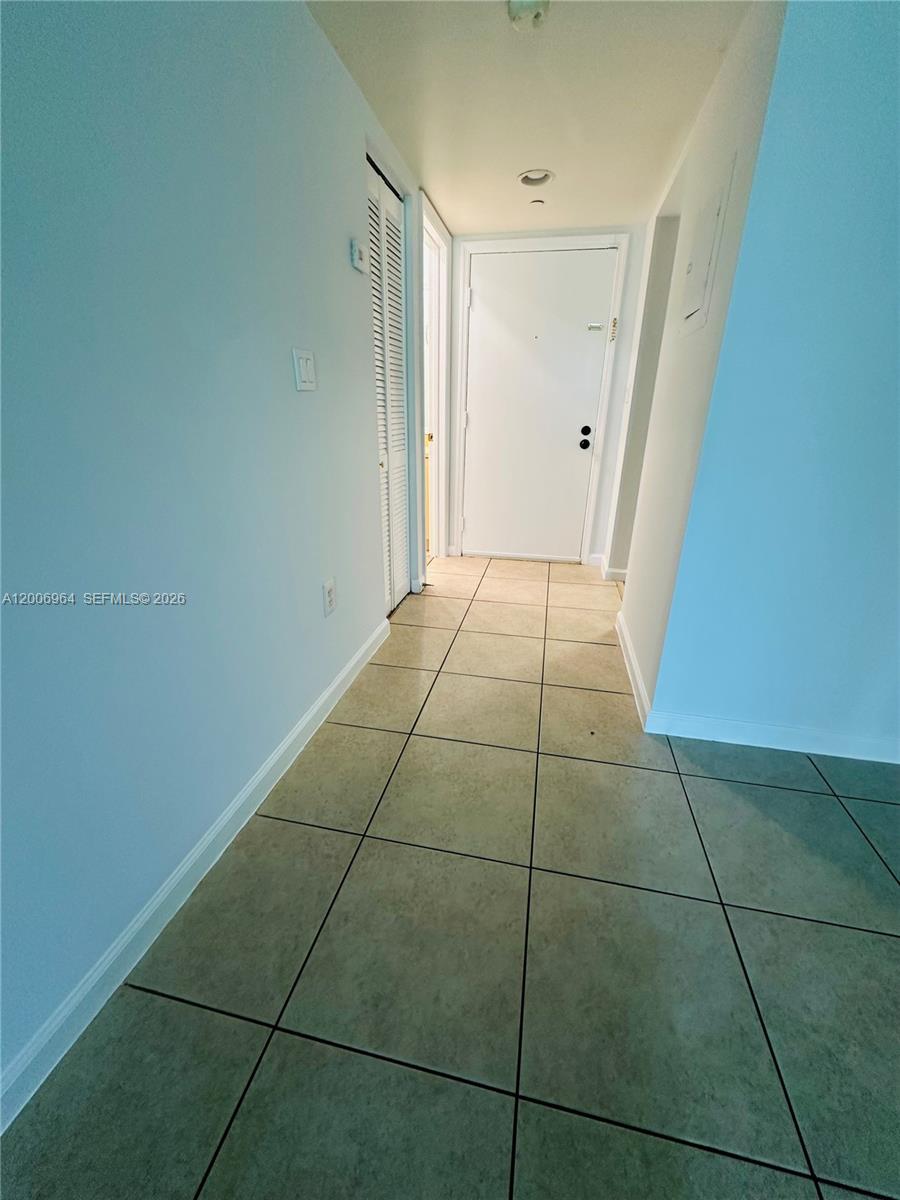 A hallway with light-colored walls and large square floor tiles leads to a white door — 8700 SW 133rd Ave Rd # 109, Miami FL 33183, MIAMI, FL