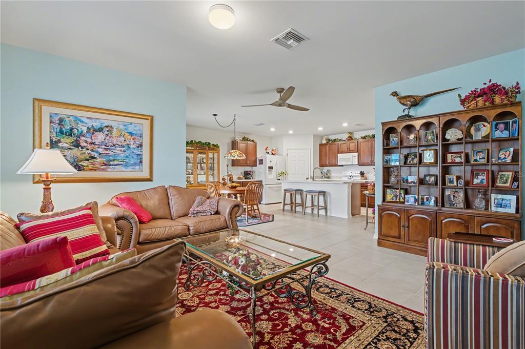 A living room with leather furniture and a large wooden bookshelf opens to a kitchen — 7025 WATERFORD PARKWAY, PUNTA GORDA, FL