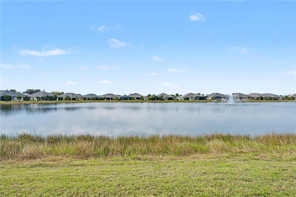 A wide view of a residential pond with a fountain and houses in the background — 7025 WATERFORD PARKWAY, PUNTA GORDA, FL