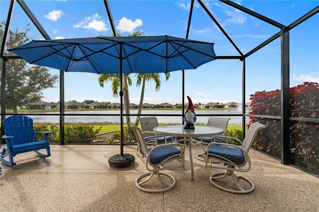 A screened-in patio features a dining set, a blue umbrella, and a lake view — 7025 WATERFORD PARKWAY, PUNTA GORDA, FL