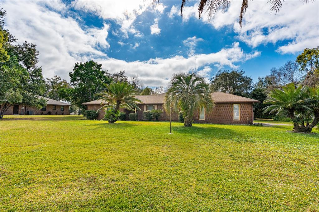 A single-story brick house sits on a large grassy lot with several palm trees — 810 HENSEL HILL ROAD W, PORT ORANGE, FL
