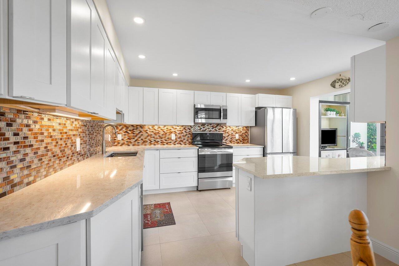A modern kitchen features white cabinetry, stainless steel appliances, and a mosaic tile backsplash — 3677 Quail Ridge Drive # B, Boynton Beach FL 33436, BOYNTON BEACH, FL