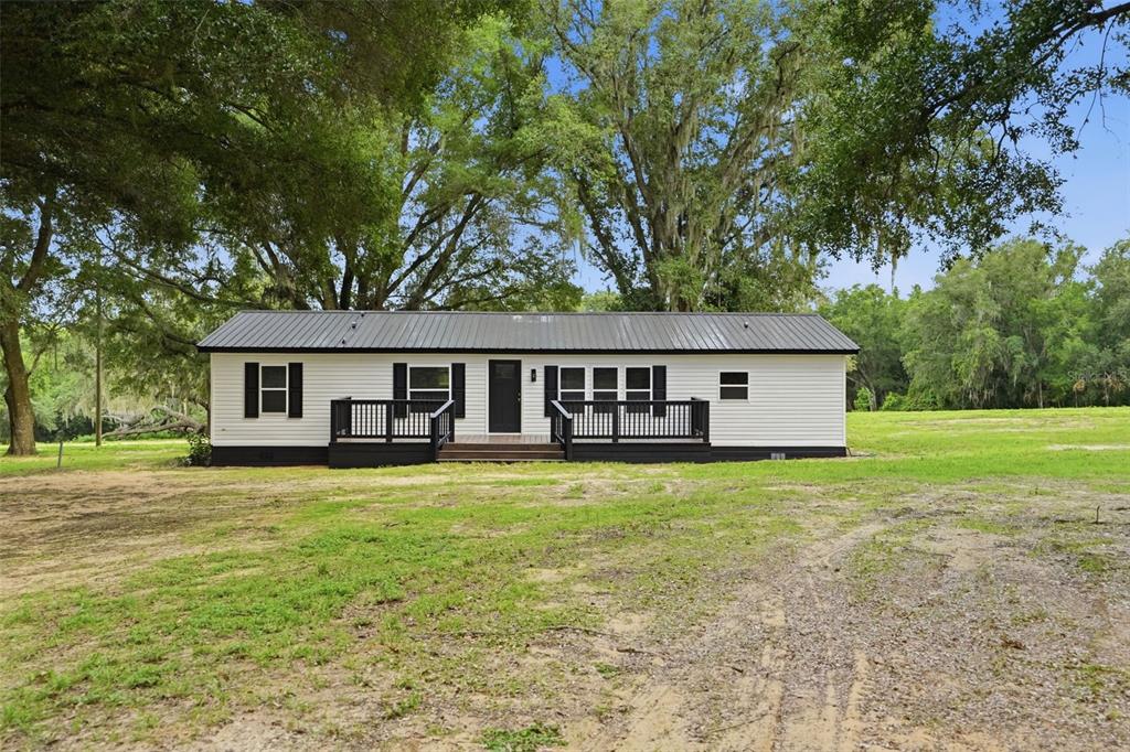A single-story house with white siding and a dark metal roof sits on a lawn — 28470 SOARING HAWK LANE, BROOKSVILLE, FL
