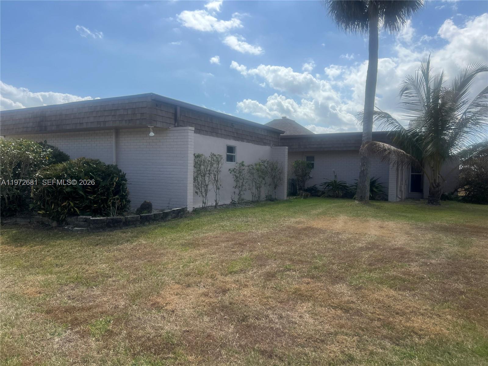 The exterior of a single-story house features light-colored brick walls and a dark shingled roof — 5724 S Bayberry Ln, Tamarac FL 33319, TAMARAC, FL