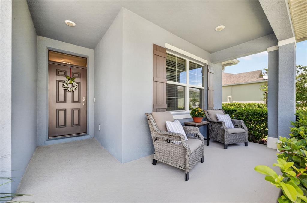 A covered front porch features two wicker chairs, a small table, and a brown door — 5264 GREENHEART AVENUE, MOUNT DORA, FL