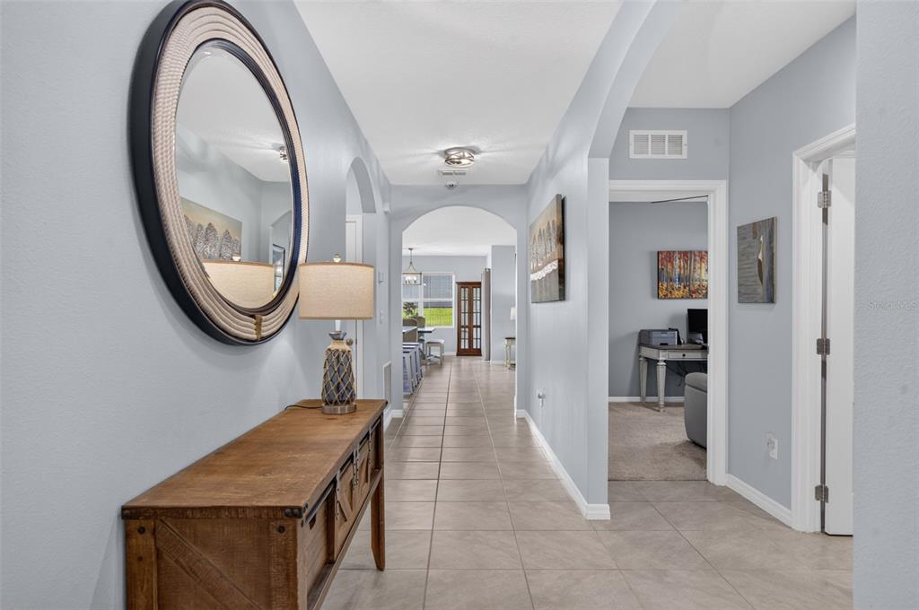 A hallway with tile flooring leads from a foyer toward an open-concept living area — 5264 GREENHEART AVENUE, MOUNT DORA, FL