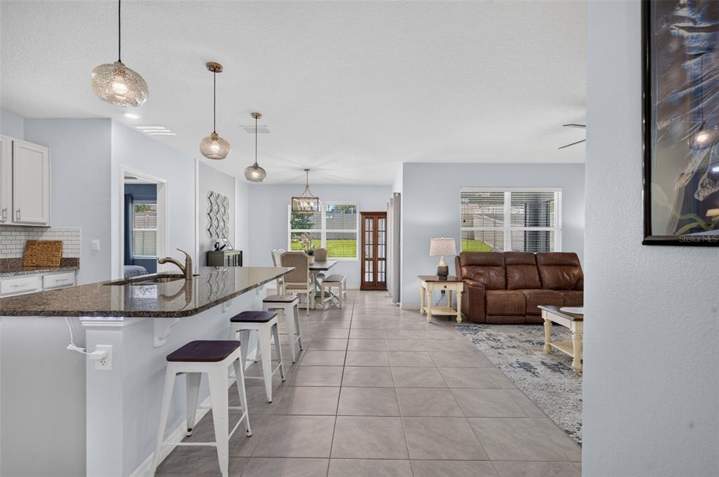 An open-concept kitchen and living area features tile flooring, a granite island, and pendant lighting — 5264 GREENHEART AVENUE, MOUNT DORA, FL