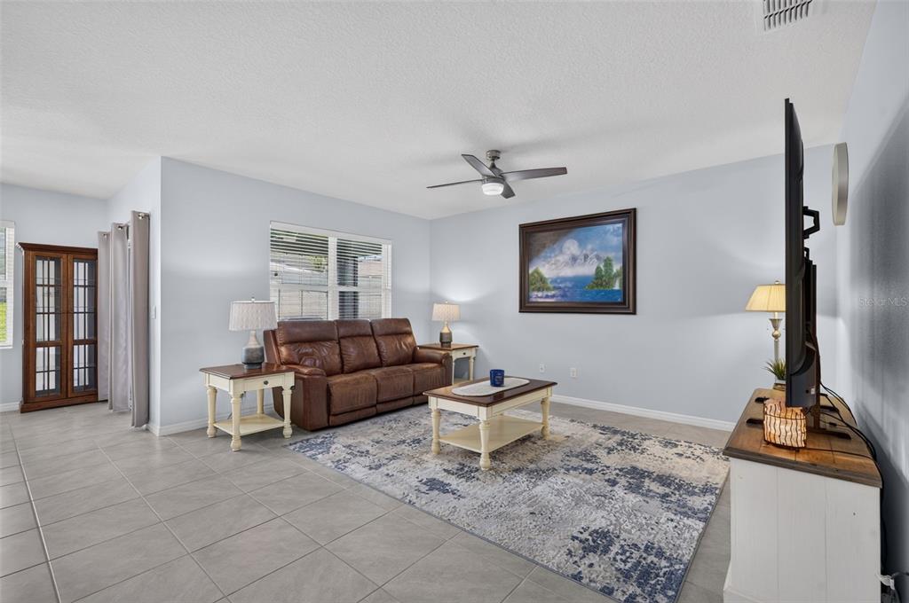 A living room with tile flooring, a brown leather sofa, and a large area rug — 5264 GREENHEART AVENUE, MOUNT DORA, FL