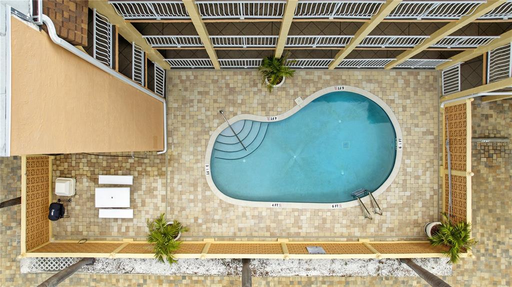 An aerial view shows a kidney-shaped swimming pool surrounded by a paved deck and fencing — 3575 GULF BOULEVARD UNIT 105, ST PETE BEACH, FL