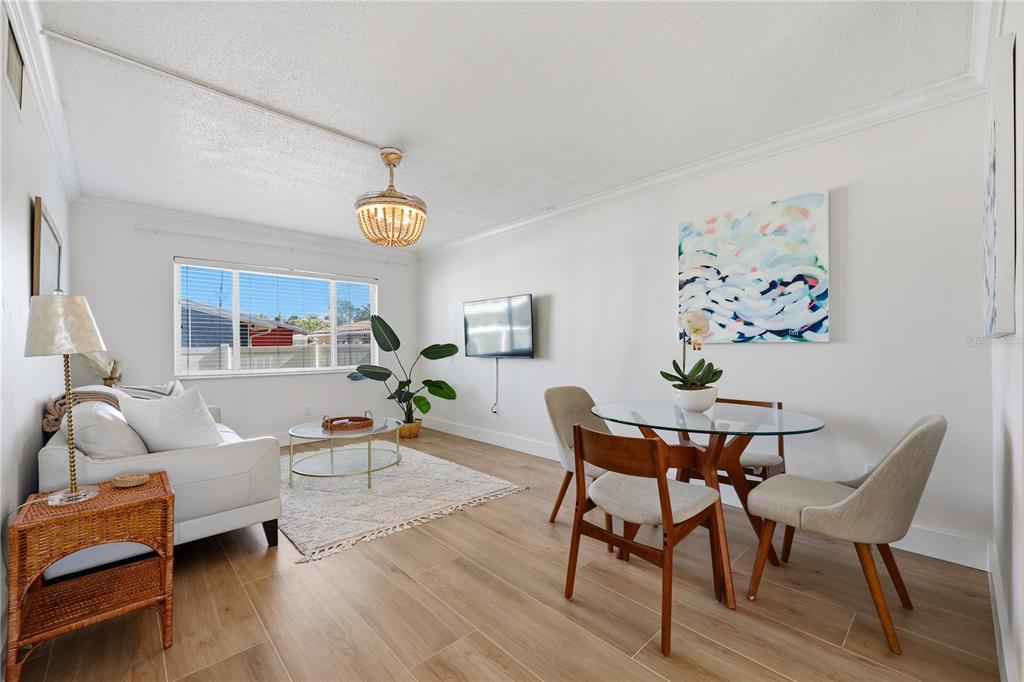 A bright living and dining area features white walls, wood-look tile flooring, and a chandelier — 3575 GULF BOULEVARD UNIT 105, ST PETE BEACH, FL