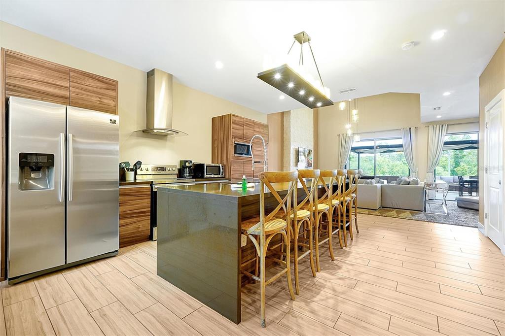 A modern kitchen features a large island with bar seating, stainless steel appliances, and wood cabinetry — 3061 ROCKEFELLER WAY, KISSIMMEE, FL
