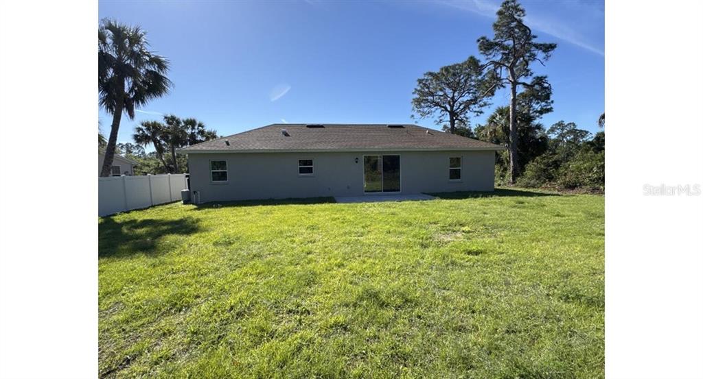 The rear exterior of a single-story house features a sliding glass door and lawn — 3467 INVERNESS STREET, NORTH PORT, FL