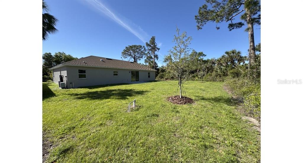 The exterior of a single-story house features a gray stucco facade and a grassy backyard — 3467 INVERNESS STREET, NORTH PORT, FL