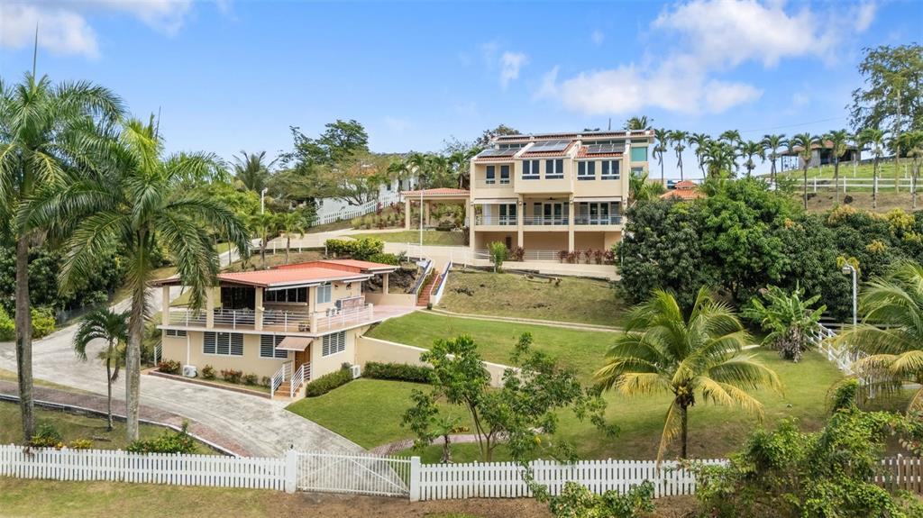 A multi-level house with a white picket fence and palm trees on a grassy hill — 23 & 24 HACIENDA CARABALI, LUQUILLO, PR