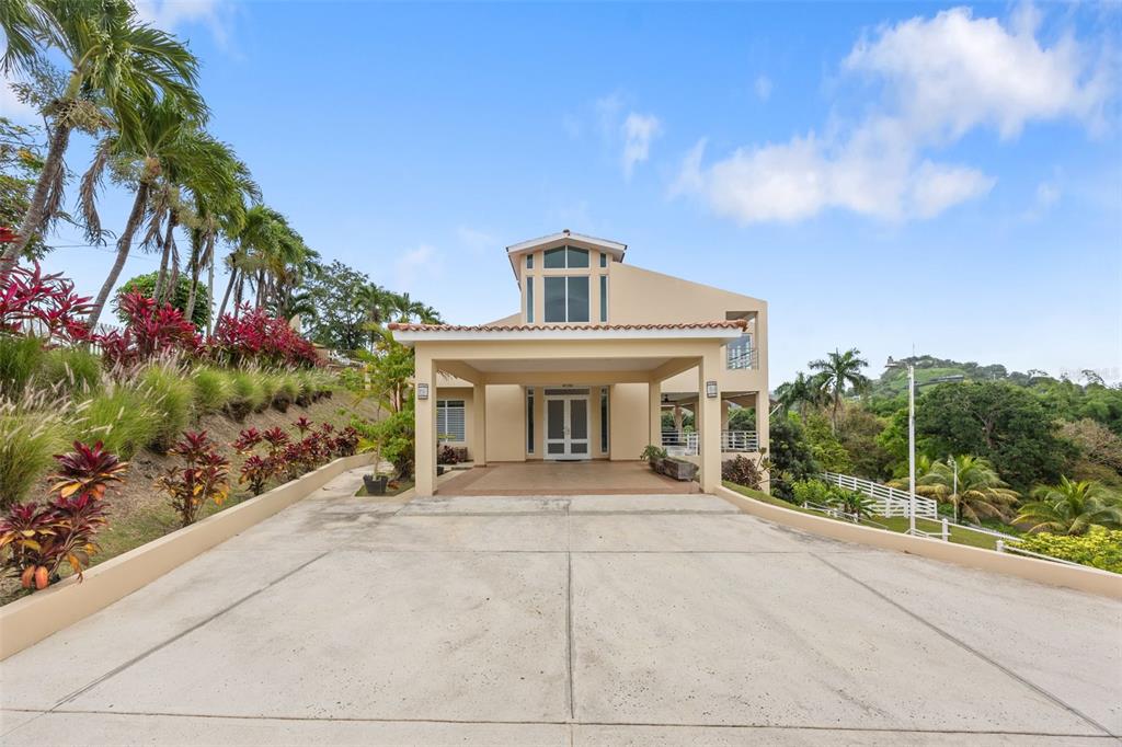 A beige house with a large concrete driveway and a covered entryway under a blue sky — 23 & 24 HACIENDA CARABALI, LUQUILLO, PR