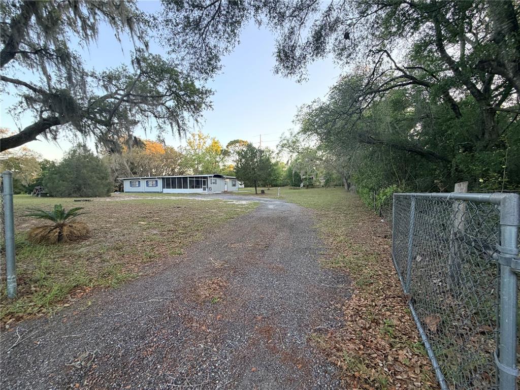 A gravel driveway leads to a single-story house surrounded by trees and a chain-link fence — 4880 N HIGHLAND PARK DRIVE, HERNANDO, FL