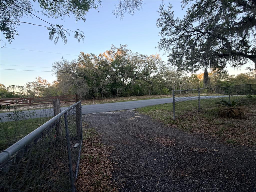 A gravel driveway leads to a paved road bordered by trees and chain-link fencing — 4880 N HIGHLAND PARK DRIVE, HERNANDO, FL