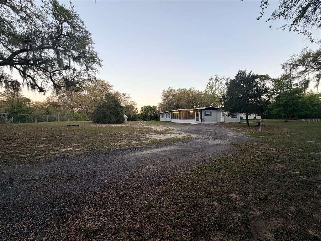 A single-story manufactured home sits on a large, grassy lot with a gravel driveway — 4880 N HIGHLAND PARK DRIVE, HERNANDO, FL