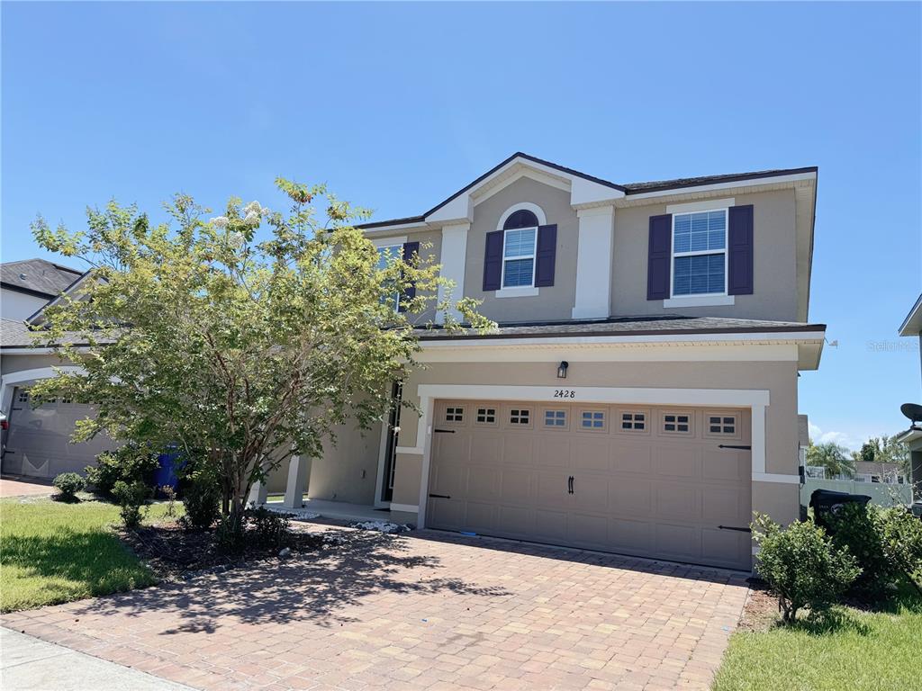 A two-story suburban house features a tan stucco exterior, dark shutters, and a paved driveway — 2428 CHATEAU LOOP, KISSIMMEE, FL