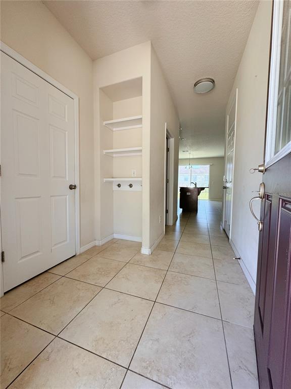 An entryway with tile flooring features a built-in shelving nook and a view toward the kitchen — 2428 CHATEAU LOOP, KISSIMMEE, FL