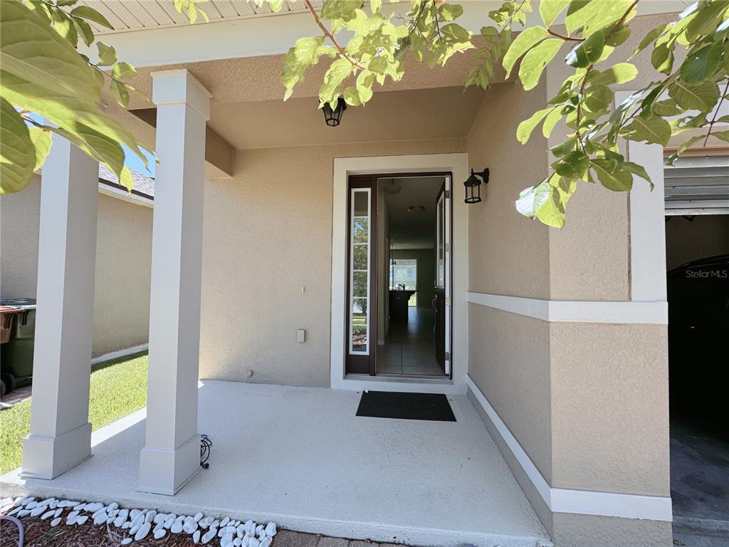 A covered concrete porch leads to an open front door revealing an interior hallway — 2428 CHATEAU LOOP, KISSIMMEE, FL