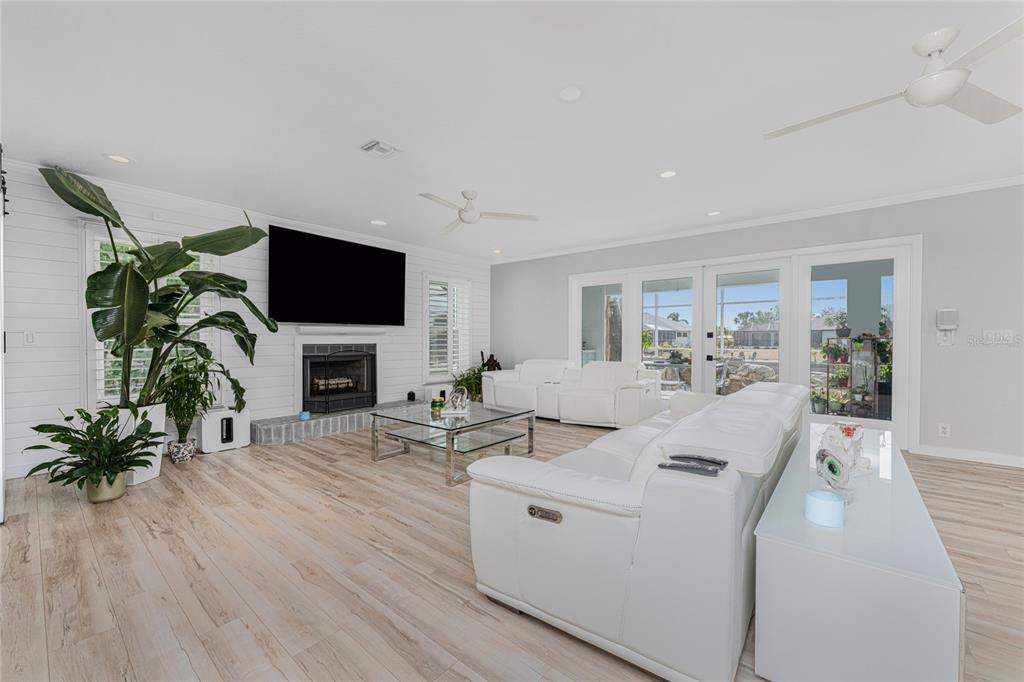 A bright living room features white leather sofas, a fireplace, and light wood-look flooring — 139 SEVILLE PLACE SW, PORT CHARLOTTE, FL