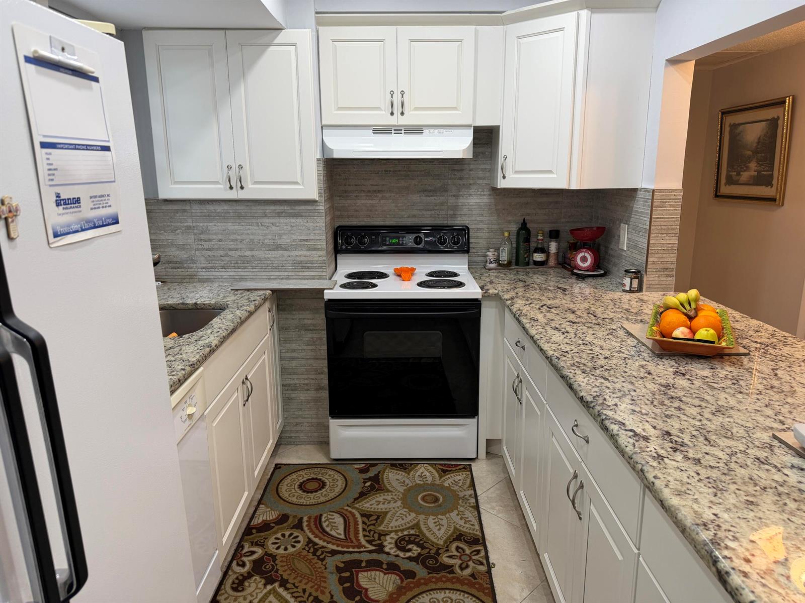 A kitchen features white cabinets, granite countertops, a white stove, and a patterned area rug — 701 Lori Drive # 204, Palm Springs FL 33461, PALM SPRINGS, FL