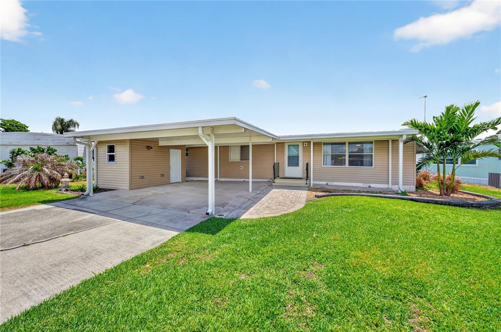 A single-story house with tan siding, a carport, and a paved walkway in the front — 957 TODD WAY, TAVARES, FL