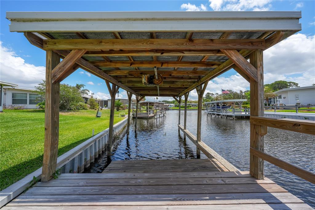 A wooden boat lift with a metal roof extends over a canal between two houses — 957 TODD WAY, TAVARES, FL