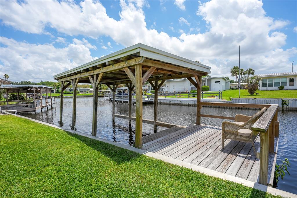 A wooden boat dock with a covered slip and a seating area sits on a canal — 957 TODD WAY, TAVARES, FL