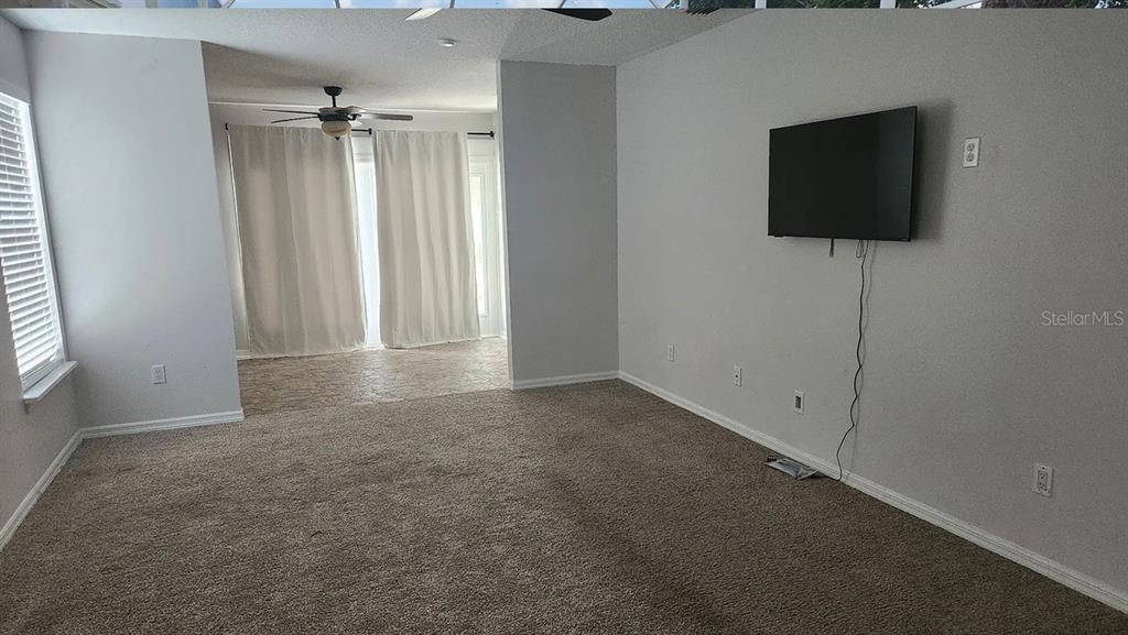 A carpeted living room features a wall-mounted television and a doorway leading to a sunroom — 4303 INWOOD LANDING DRIVE, ORLANDO, FL