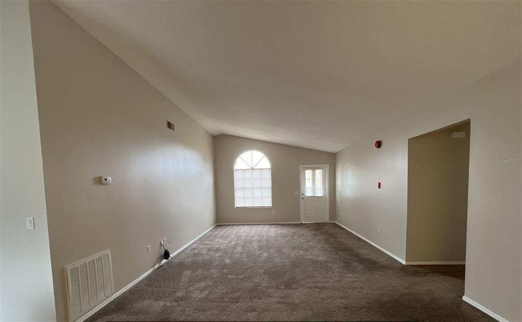 An empty living room features beige walls, brown carpeting, a vaulted ceiling, and a window — 319 OAK TRACK DRIVE, OCALA, FL
