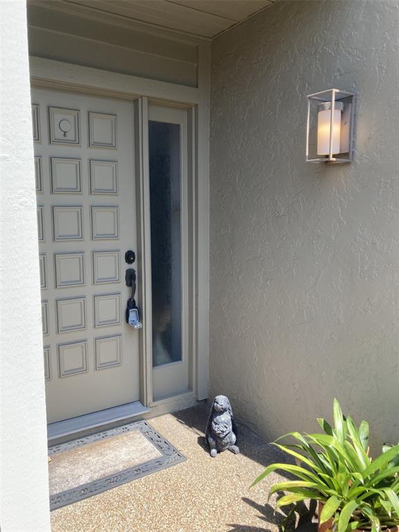 A beige front door with a side window, a wall sconce, and a rabbit statue — 3407 AVENIDA MADERA UNIT A, BRADENTON, FL
