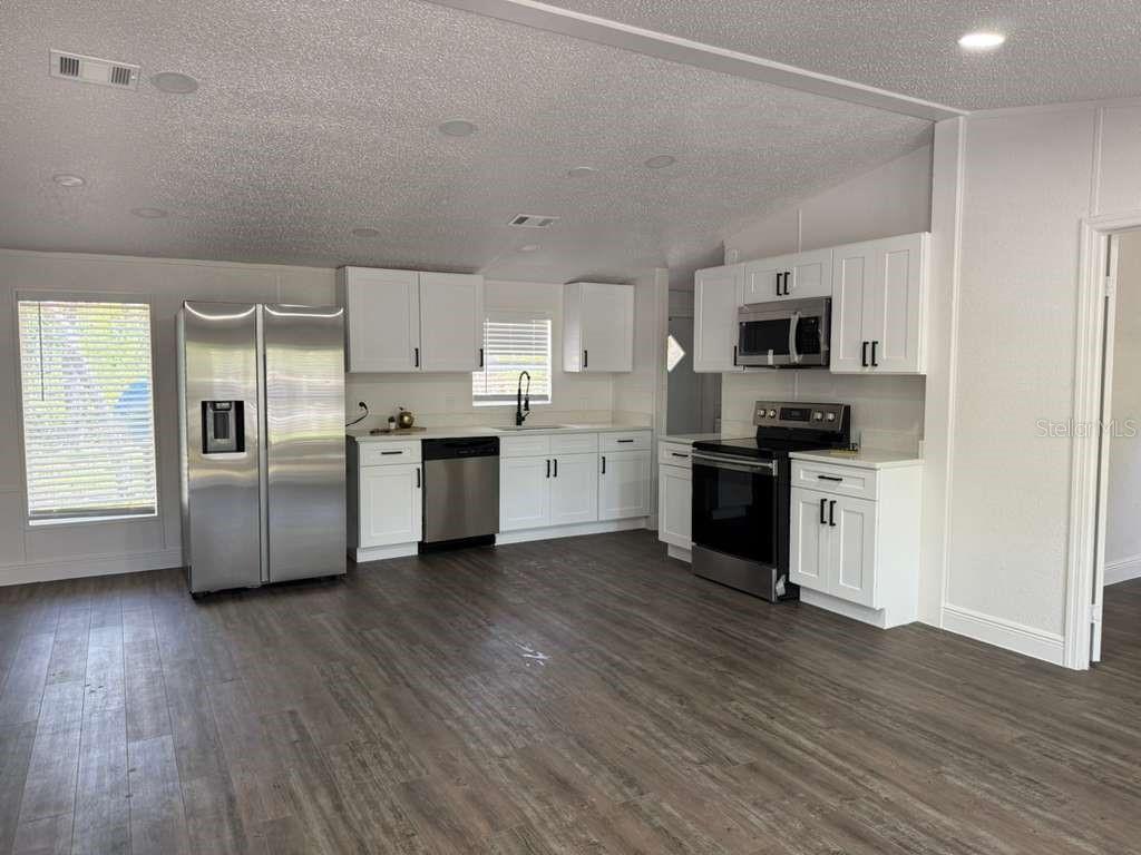 A kitchen features white cabinets, stainless steel appliances, and wood-look flooring — 10350 EVERGREEN STREET, NEW PORT RICHEY, FL